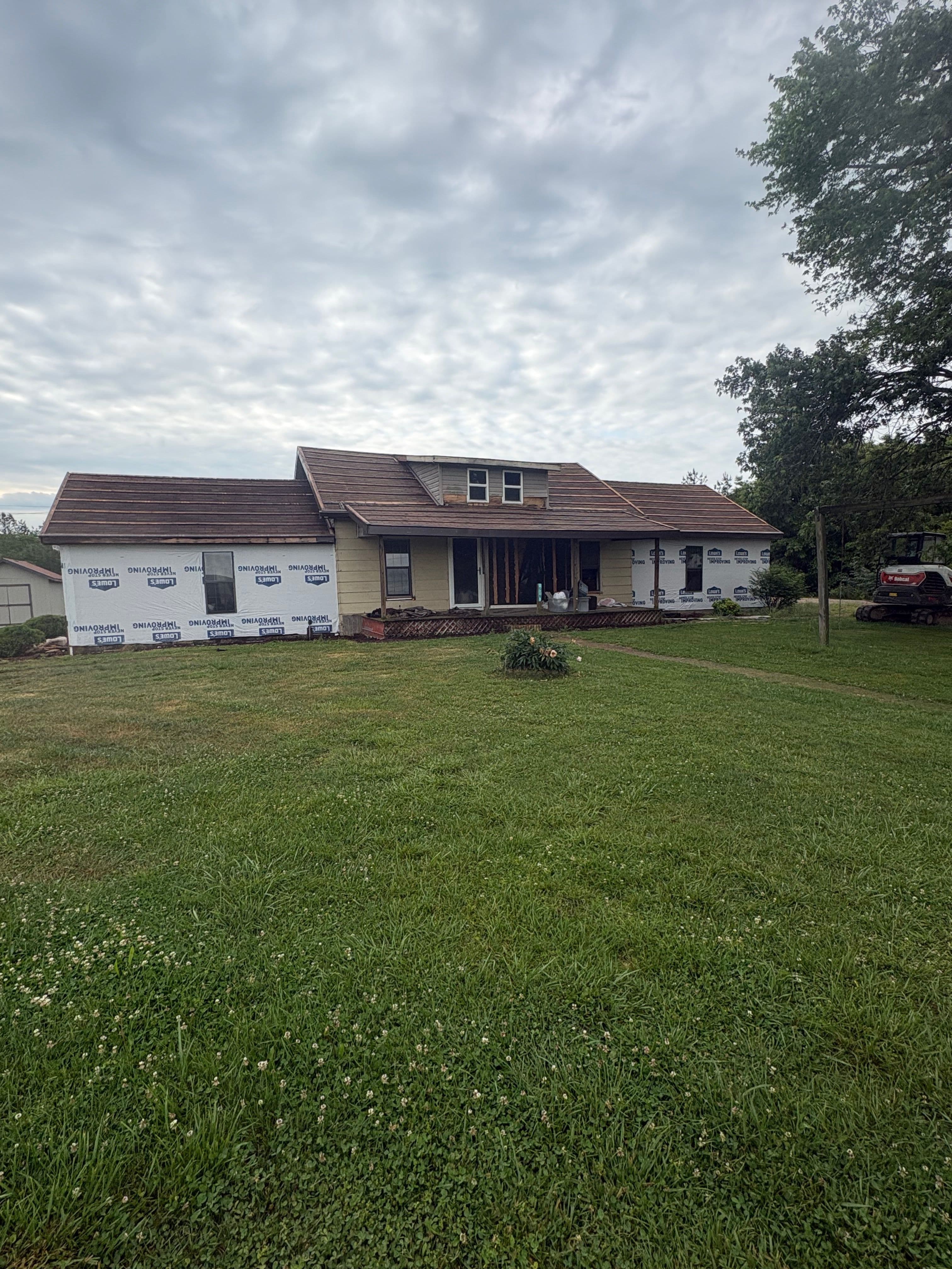 House undergoing renovation with new siding, surrounded by a green lawn and cloudy sky.